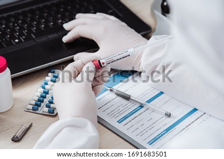 The microbiologist enters the data into the computer after coronavirus test. Analysis of test tube with a sample. Tube of biological sample contaminated by Coronavirus. Positive results. Medical exam. Royalty-Free Stock Photo #1691683501