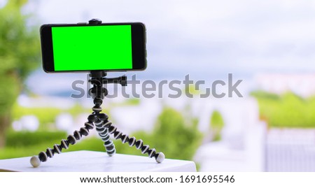 Smartphone on a tripod with green screen on it. mobile smart phone with chroma key green screen on blurry city background, new technology concept. Using the tripod to hold the mobile phone