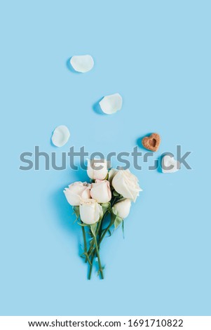 Vertical morning card. White roses on a blue background with scattered petals and two pieces of sugar in the shape of hearts.