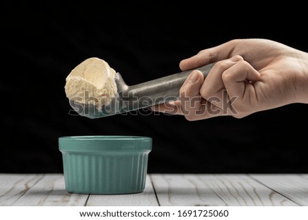 A scoop of vanilla ice cream in a metal ice cream scoop over a bowl.