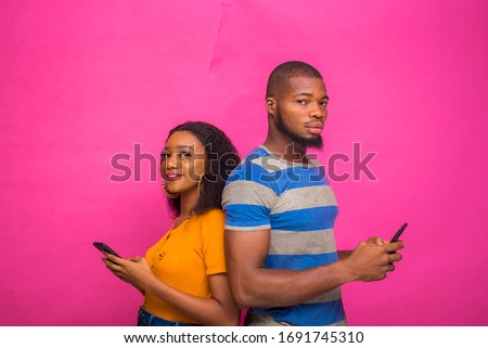 two young africans isolated over pink background backing each other as they operate their smartphone, telephone, cellphone.
