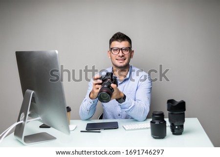 Top view serene bearded photographer watching at camera while holding it in arms in office. Image concept