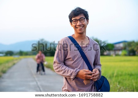 Portrait of an Asian Thai man looking humble and relaxed into the camera, surrounded by rice fields and in the background there is an unknown person riding a bicycle Royalty-Free Stock Photo #1691758882