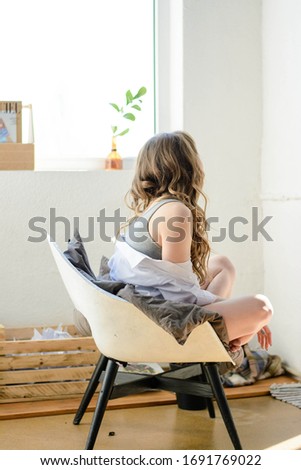 Beautiful girl with long brown hair in tee and white shirt sitting on the chair.