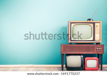 Retro classic old analog TV receivers set and aged wooden television stand with outdated amplifier front gradient mint blue wall background. Broadcasting, news concept. Vintage style filtered photo