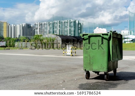 A green rubbish bin in a car park with view of residential area and blue sky behind Royalty-Free Stock Photo #1691786524