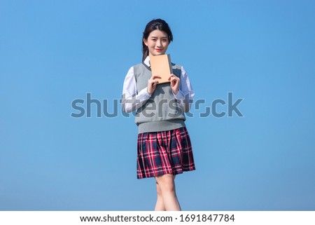 Asian schoolgirl with a book in her hand against a blue sky background

