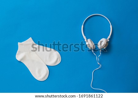 White sports socks and white headphones on a blue background. The color trend. The concept of music and sports. Flat lay.