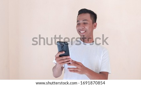 Wow face of Young Asian man shocked what he look on the smartphone while gaming, watching the movie, or read a massage, or texting. Indonesia Man wear white shirt Isolated pink background.