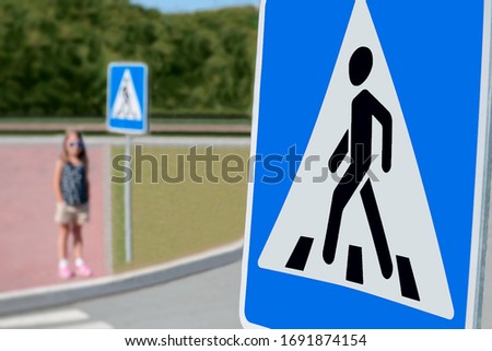 Square road warning sign with man walking symbol. Signal with black doll in black on a blue background. School child is standing near the pedestrian crossing on the street. Traffic rules for children