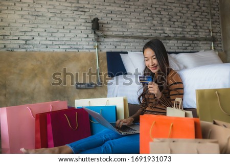Young asian woman with smart mobile phone and laptop computer using credit card for shopping online in bedroom