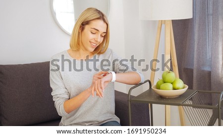 Beautiful blonde in a light gray blouse. Smart watch on the girl's hand. Green apples on the coffee table.