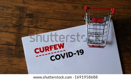 Shopping in coronavirus time concept. Shopping cart with word Curfew, COVID-19 on wood background.