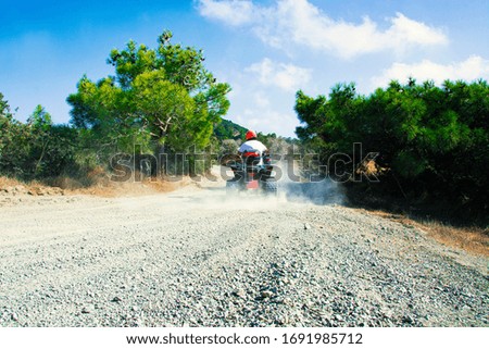 Man Driving His Quad Bike on a Dirt Road in the Forest. Summertime and Clean sky in the background.