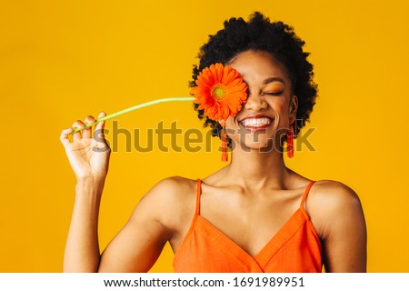 Portrait of a happy young woman holding orange Gerbera daisy covering her eye with eyes closed Royalty-Free Stock Photo #1691989951