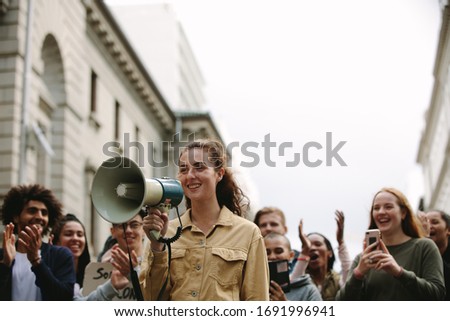 Young woman with group of people in a rally. Woman with a megaphone outdoors on road during a protest.