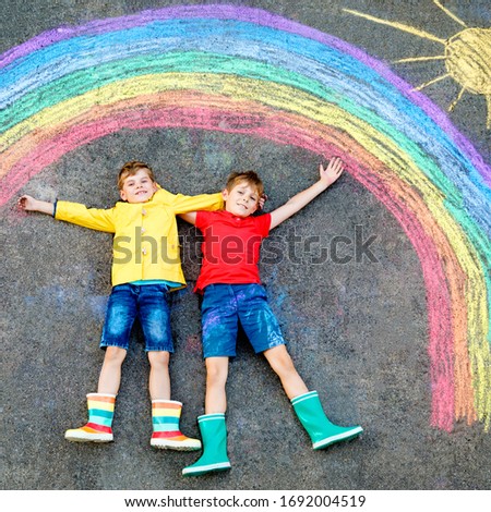 two school kids boys with rainbow painted with colorful chalks on ground during pandemic coronavirus quarantine. Children painting rainbows along with the words Let's all be well.