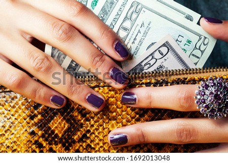 pretty fingers of african american woman holding money closeup with purse, luxury jewellery on python clutch, cash for gifts