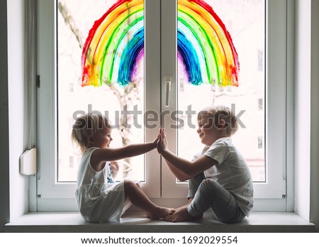 Little children on background of painting rainbow on window. Photo of kids leisure at home. Positive visual support during quarantine Pandemic Coronavirus Covid-19 at home. Family background