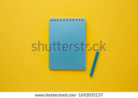 Blue blank notebook for your inscription with a blue pencil on a yellow background.