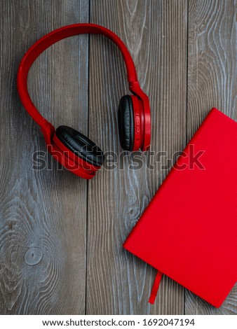 
Red headphones and a red notebook on a wooden background. Place for advertising. Wireless headphones and notepad.