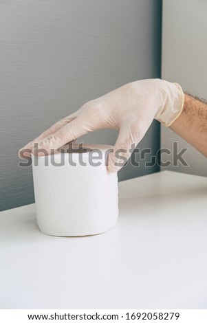 A medical worker in rubber latex glove on his hand holds toilet paper roll . Concept of coronavirus panic. Isometric and geometric style in the corner. 