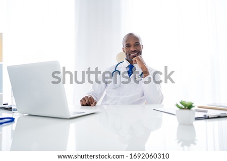 Photo of family doc dark skin guy online consultation use notebook tell write give prescriptions help people control panic risk epidemic wear white lab coat sit chair office clinic indoors
