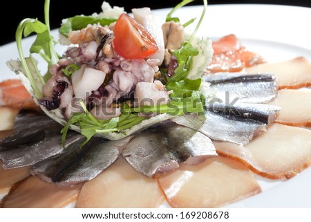macro sliced assorted fish and seafood on a white plate on a black background studio