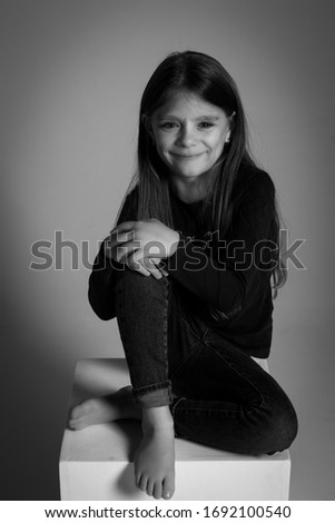 Happy little girl laughing sitting on a pedestal. Charismatic black and white close-up portrait in a photo Studio. Solid color background.