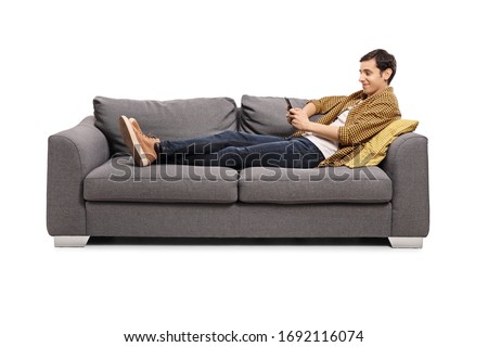 Relaxed young man lying on a sofa with a mobile phone isolated on white background Royalty-Free Stock Photo #1692116074