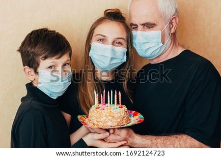 grandfather and grandchildren in protective masks are holding a birthday cake with candles forced to celebrate the holiday away from friends in isolation. Quarantined due to an epidemic of coronavirus