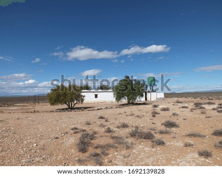 White farm house in the karoo with blue sky and white clouds in the background with trees forming an oasis