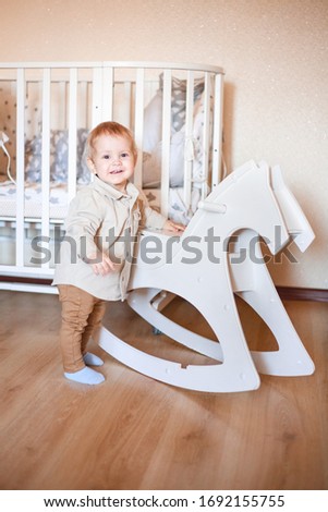 a one year old child stands next to a wooden horse in his room