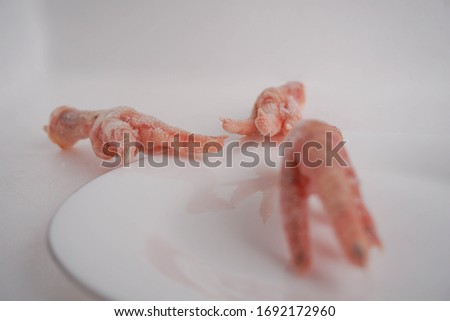 3 chicken legs / paws with ice on a white plate, on a white background