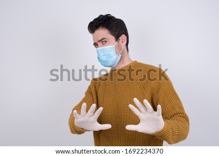 Handsome young man over isolated background afraid and terrified with fear, and disgusted expression stop gesture with both hands saying: Stay there. Panic concept.  Protection against disease.