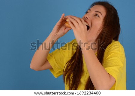 woman in yellow t-shirt bites a hamburger on a blue background