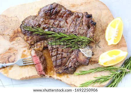 Marble beef grilled with lemon and rosemary on a wooden board on a light background. Slice of meat with a fork. Background image, copy space