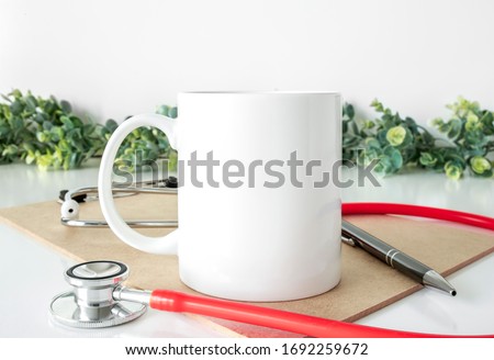 Blank 11oz white coffee mug on white background with stethoscope and clipbards, nurse/doctor mug mockup Royalty-Free Stock Photo #1692259672