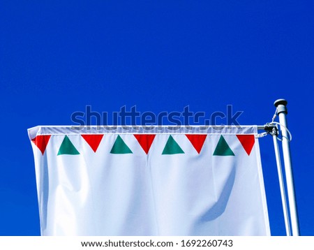 waving white, red and green shiny flag in strong wind on silver color metal pole. blue sky and white cloud. blue sky concept. abstract low angle view.  