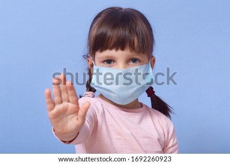Close up portrait of caucasian little girl wearing medical face mask and making stop sign with her palm. Social distancing, self isolation, coronavirus, covid 19, virus, epidemic, pandemic concept.