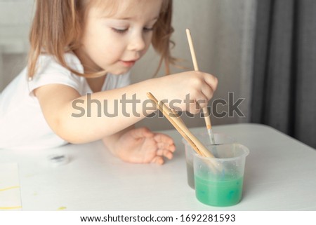 4 years old girl washes a paint brush in a jar of colored water. children's creativity during the period of self-isolation and quarantine in connection with the coronavirus