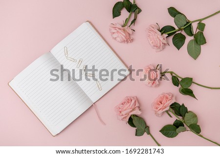 Notebook on a pastel pink background with gold paper clips and pink roses. The concept of study, education, office workplace. Top view. 
