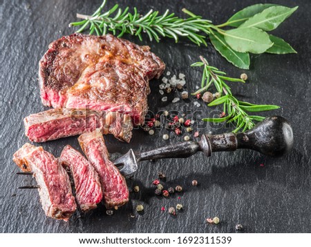 Grilled medium rare rib eye steak with herbs and seasoning on gray stone background. Picture of delicious food ready to eat.