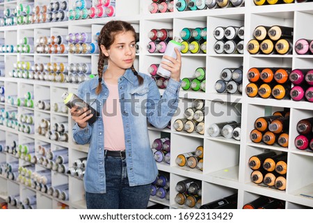 Portrait of  cheerful positive girl choosing paint color in aerosol can in art shop Royalty-Free Stock Photo #1692313429