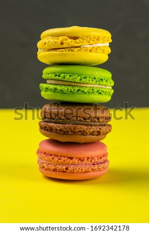 Multi-colored macaroons stand in a pile on a yellow table near a black background. Close-up