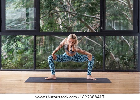 Concentrated young adult sporty woman making yoga exercise in fitness class, stretch body and training on mat against natural plants on background