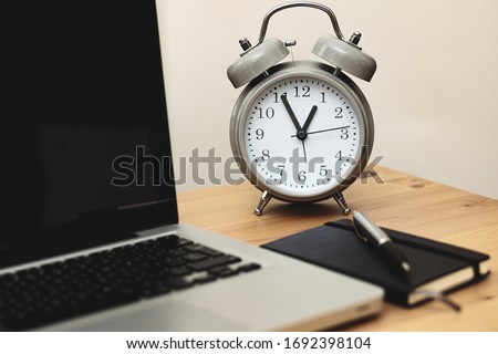 alarm clock alongside laptop and notebook in a workspace, time management concept, work from home Royalty-Free Stock Photo #1692398104