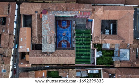 Aerial photo of playgrounds in the middle of antique city of Cusco, Peru. Basketball court and football court next to each other, surrounded by ancient school campus.
