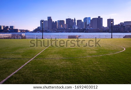 Boston city skyline in the distance across a city soccer field and water