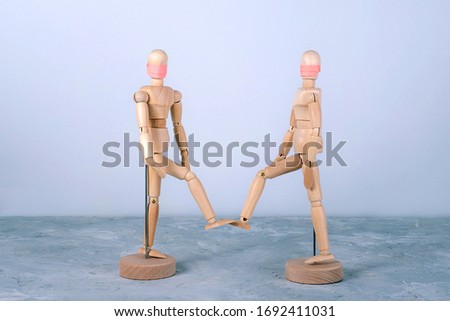 Wooden dummies in medical masks greet each other by feet touching. No handshake during COVID-19 pandemic outbreak. Self hygiene and Social distancing concept.